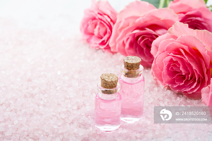 Two bottles with rose oil, spa salt crystals and pink roses.