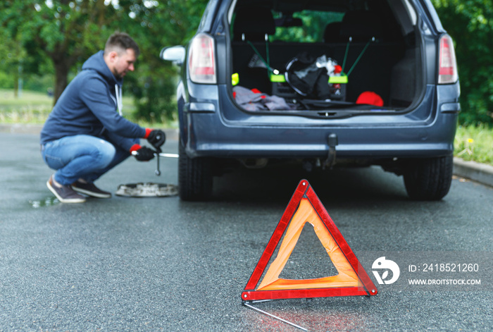 Warning triangle and man changing car wheel