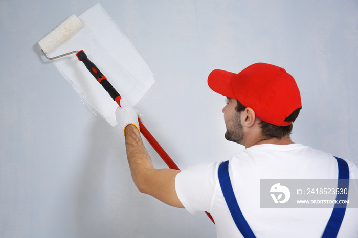 Young worker painting wall in room