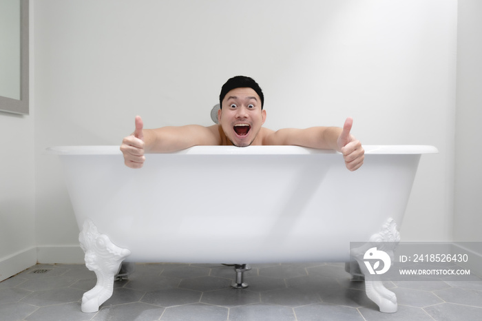 Happy funny Asian man relax and bath in a white bathtub.