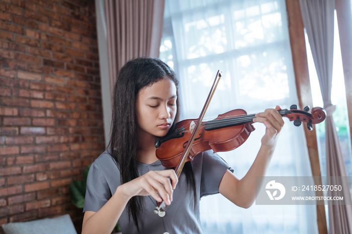 亚洲女孩独自在窗帘窗背景下的房间里拉小提琴