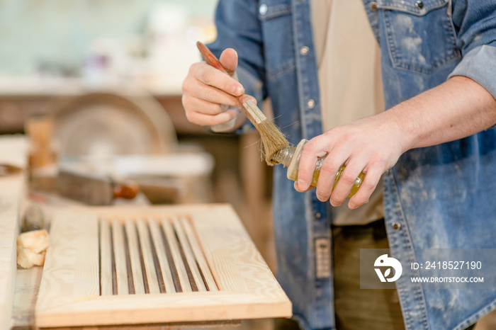 Close up man applies varnish on wooden board with paintbrush in  carpentry workshop