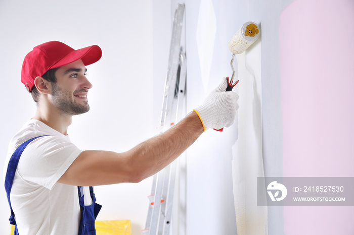 Young worker painting wall in room