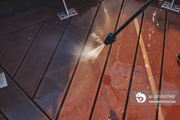 man cleaning terrace with a power washer - high water pressure cleaner on wooden terrace surface