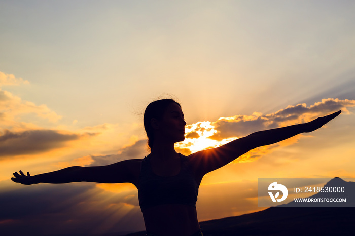 Silhouette of young woman practicing yoga or pilates at sunset or sunrise in beautiful mountain loca