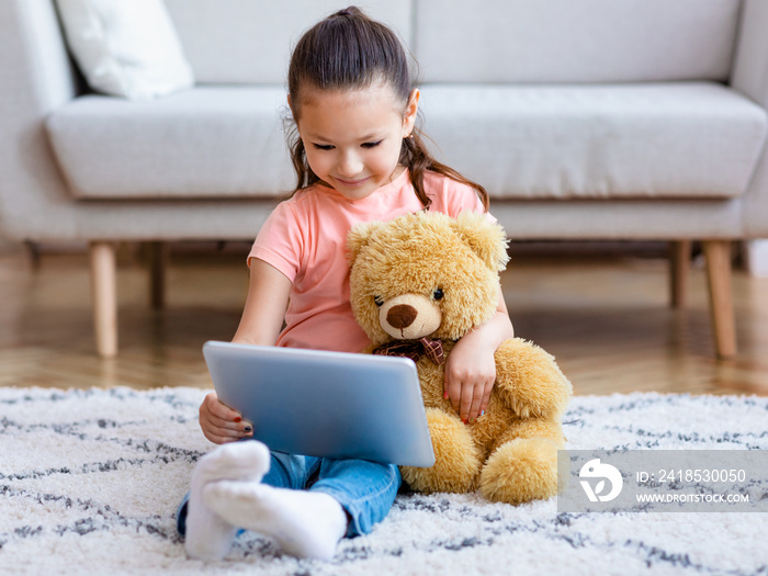 在平板电脑上看漫画的女孩在家拥抱泰迪熊