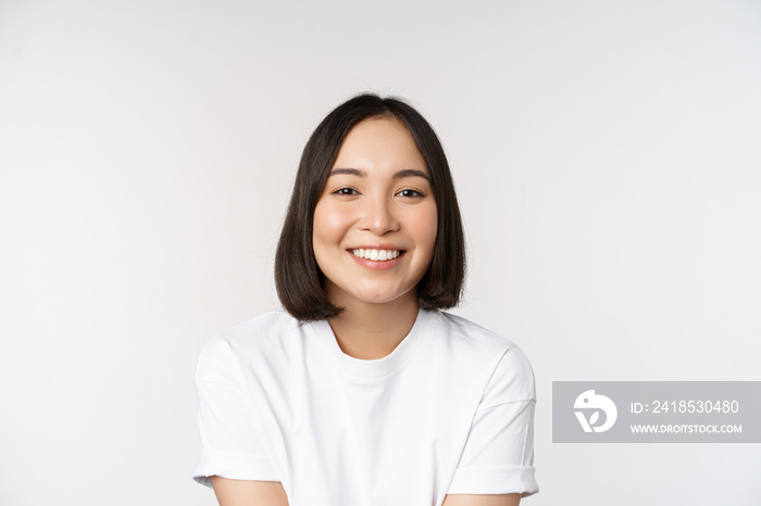 Beautiful korean girl smiling, white teeth, looking lovely at camera, standing in white tshirt over 