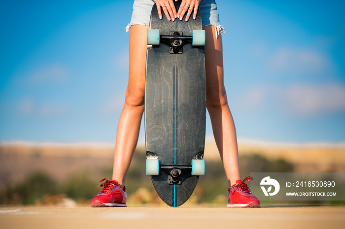 Stylish fit and sporty woman with beautiful legs and in red sneakers holds skateboard between her le