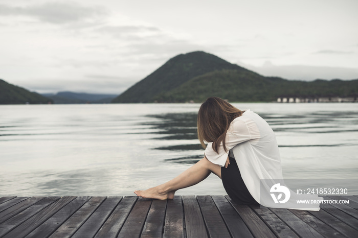 Lonely woman sitting on wooden pier and looking at the lake