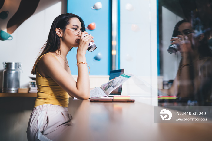 Contemplative female journalist in optical eyewear for vision protection drinking morning coffee and