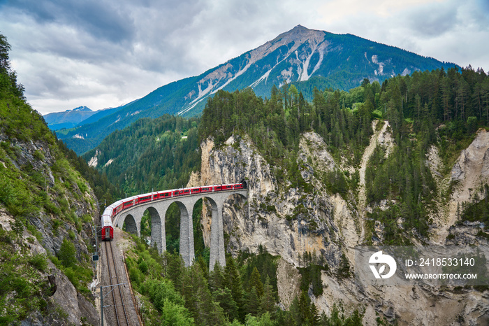 Red train passes above the Landwasser Viaduct bridge, in canton of Graubünden, Switzerland. Bernina 