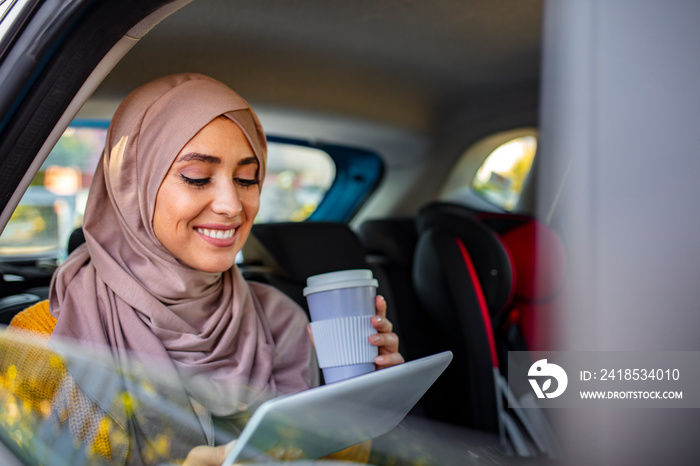 Beautiful muslim arabian woman with hijab sitting on backseat in luxury car. She drinking coffee to 