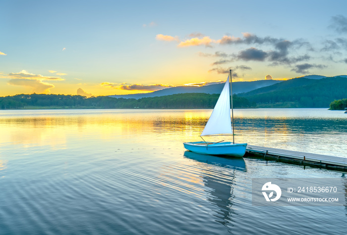 Lonely sailboat in the beautiful sunset with sun stars shines from sky and the surface of the lake i