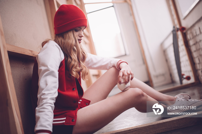 Stylish hipster woman in baseball jacket sitting with baseball ball