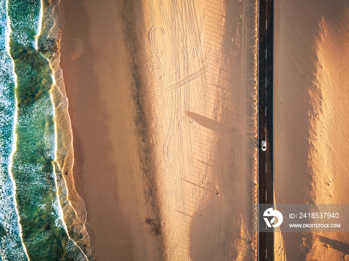 Aerial vertical view of yellow tropical sandy beach with black long way road and car traveling - oce