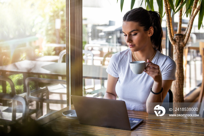 Young beautiful girl sitting at a table in a cafe by the window, drinking cappuccino coffee. Beautif