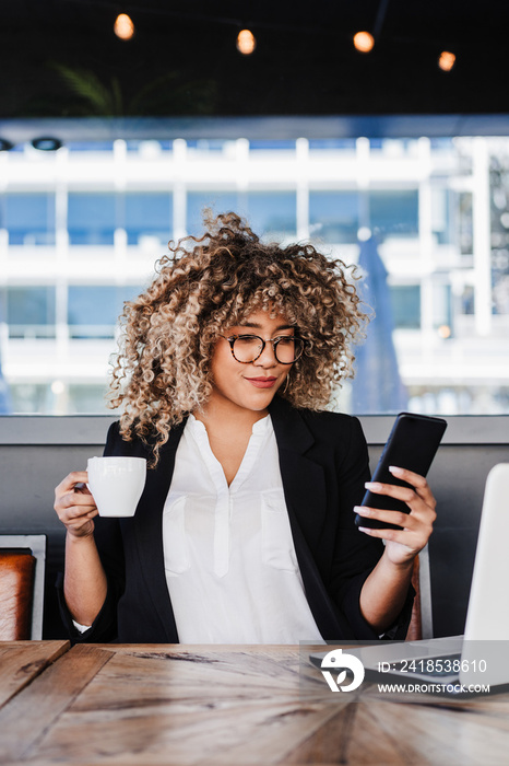 beautiful hispanic afro business woman wearing eye glasses in cafe working on laptop, mobile phone