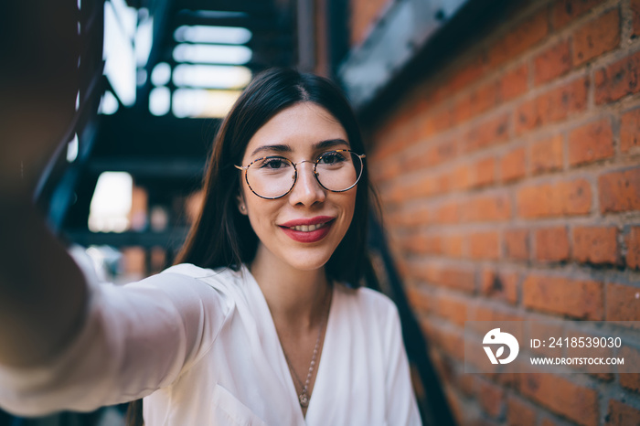 Close up portrait of charming Spanish hipster girl with cute smile on face making selfie images duri