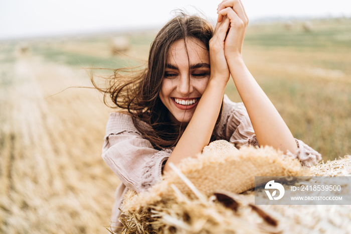 Closeup portrait of beautiful smiling woman with closed eyes. The brunette leaned on a bale of hay. 