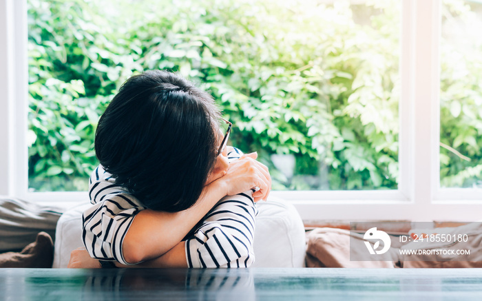 Stylish and beautiful middle aged Asian woman lie down on table in cozy living room, look out, feel 