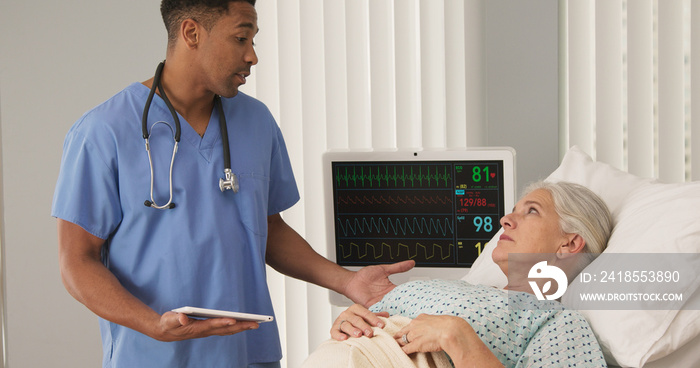 Portrait of male black nurse using tablet computer while attending ill senior patient in bed. Sick e