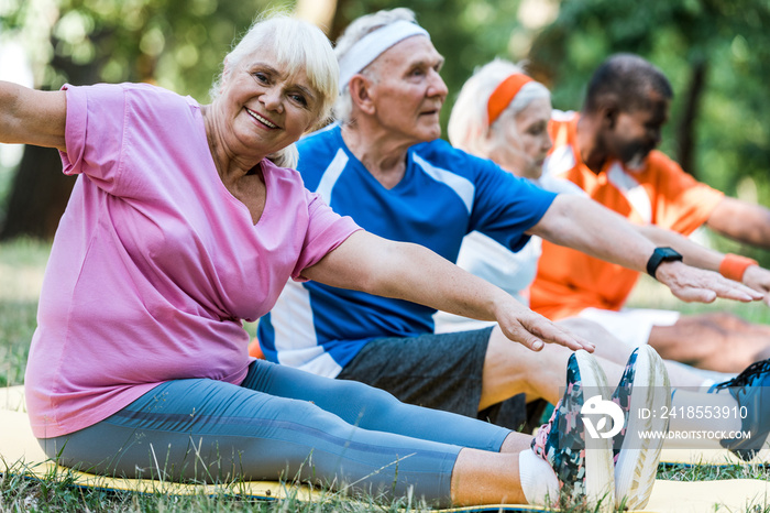 selective focus of multicultural retired men and women in sportswear sitting on fitness mats