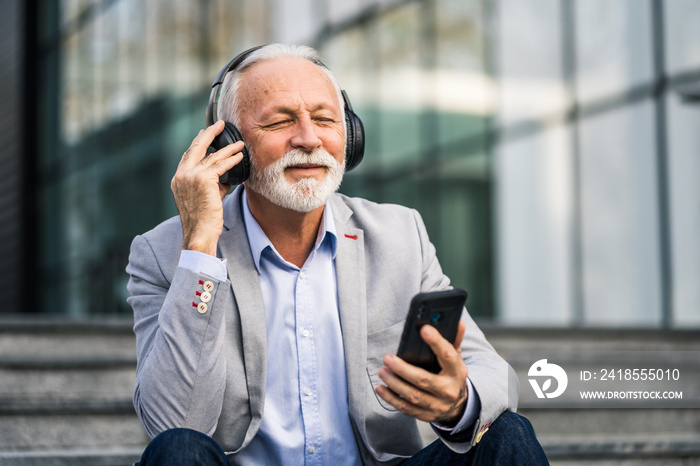 Happy senior businessman is relaxing after work in front of company building.