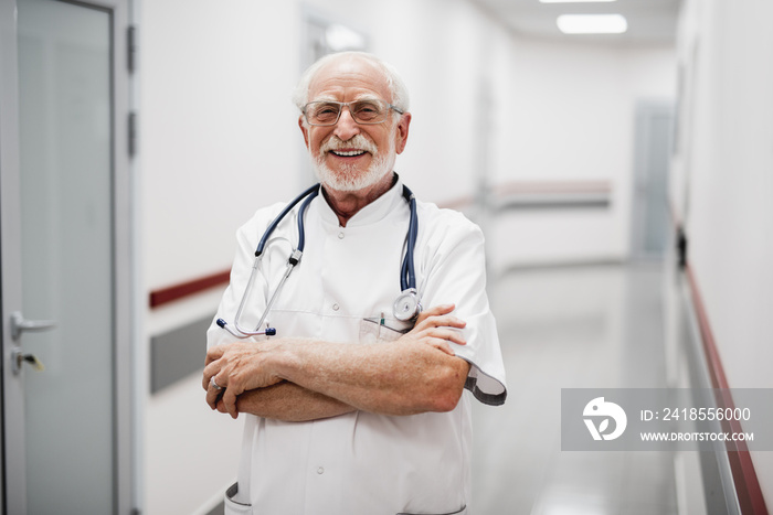 Waist up portrait of bearded gentleman in white lab coat crossing arms and looking at camera with sm