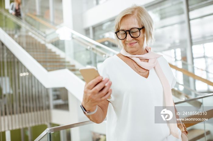 Portrait of a confident senior woman dressed in white shirt standing on the staircase of the modern 