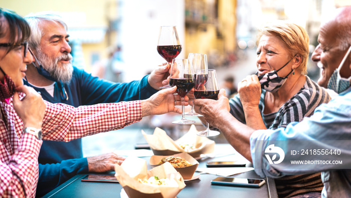 Senior couples toasting red wine at restaurant bar with face masks - New normal lifestyle concept wi