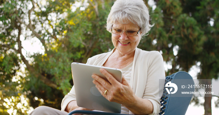 老年妇女在公园愉快地用平板电脑上网