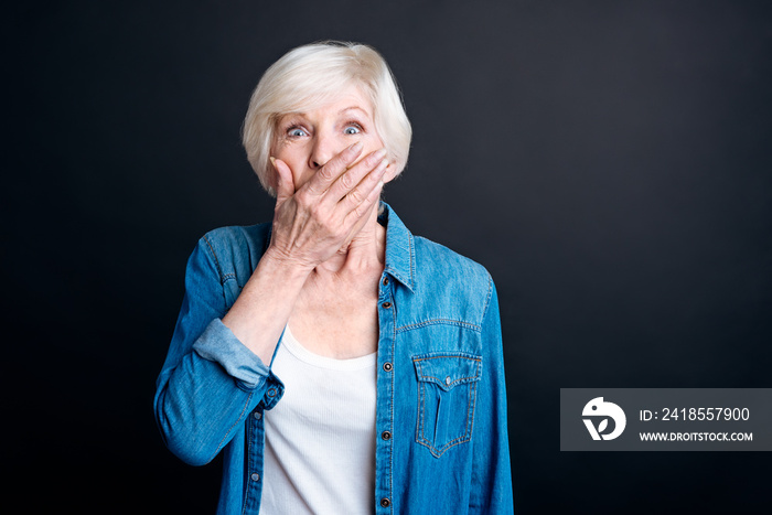 Surprised elderly woman standing on black background