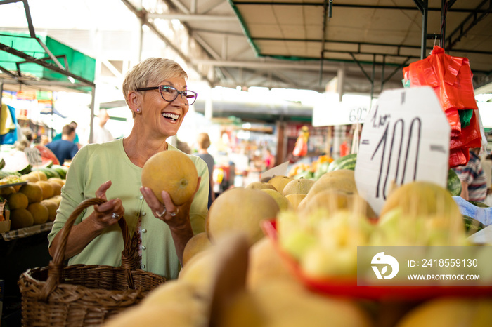 老年妇女在市场上购买新鲜有机甜瓜以获得健康营养的画像。