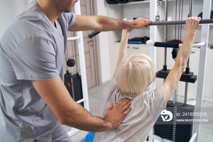 Manual therapist correcting old female posture during exercise