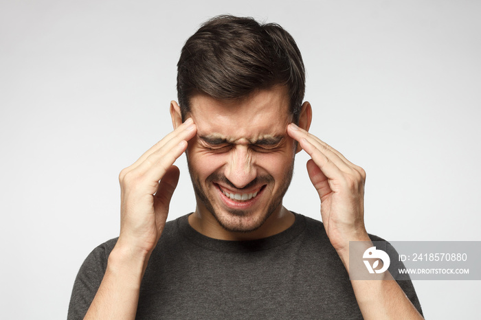 Headache concept. Young man isolated on gray background, showing how much his head hurts, experienci