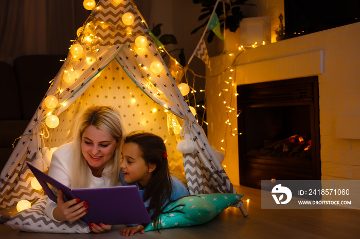 Mom with child reading book and relaxing by the fire place some cold evening, winter weekends, cozy 