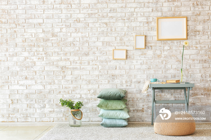 Table, pouf and soft pillows near brick wall