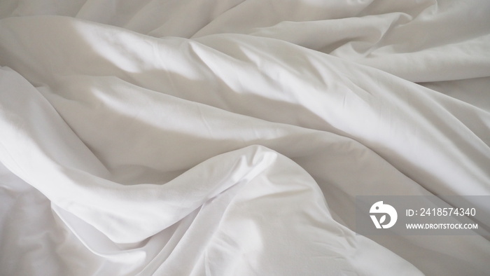 Closeup of beautiful white shiny crumpled polyester fabric sheets on the bed with warm motion and fe