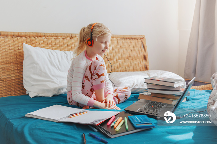 Caucasian girl child sitting in a bed and learning online on laptop Internet. Virtual class lesson o