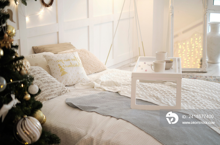 带便携式早餐桌的白色舒适现代卧室。带白色床上用品的床，圣诞树