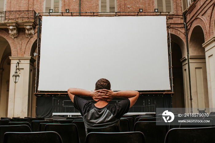 A man sits in front of a large screen. Summer theater. Open air cinema. Empty seats. Guy enjoy video
