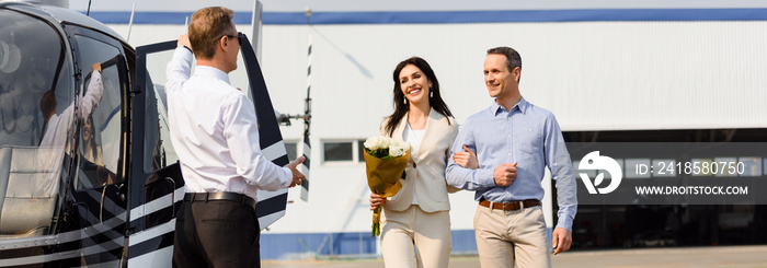 panoramic shot of happy husband and wife on romantic date near helicopter and pilot