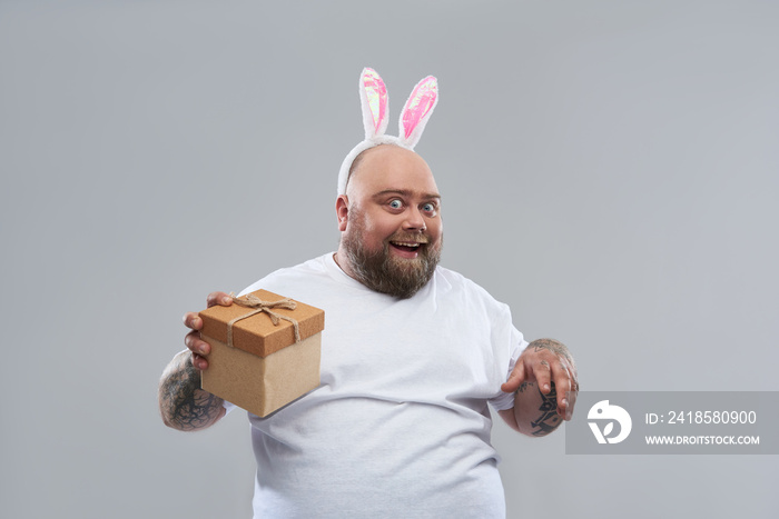 Hilarious fat man wearing bunny ears and holding gift box