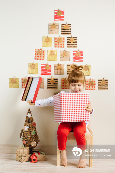 Smiling little girl opening gift box near Christmas advent calendar