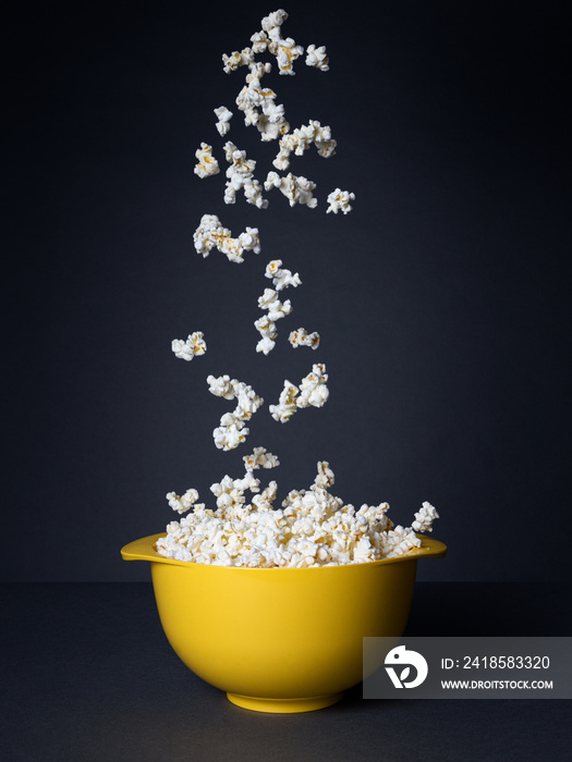 Popcorn falling into a yellow bowl on a black background