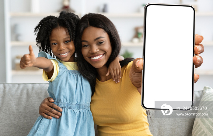 Happy Black Mother And Little Daughter Demonstrating Big Smartphone With Blank Screen