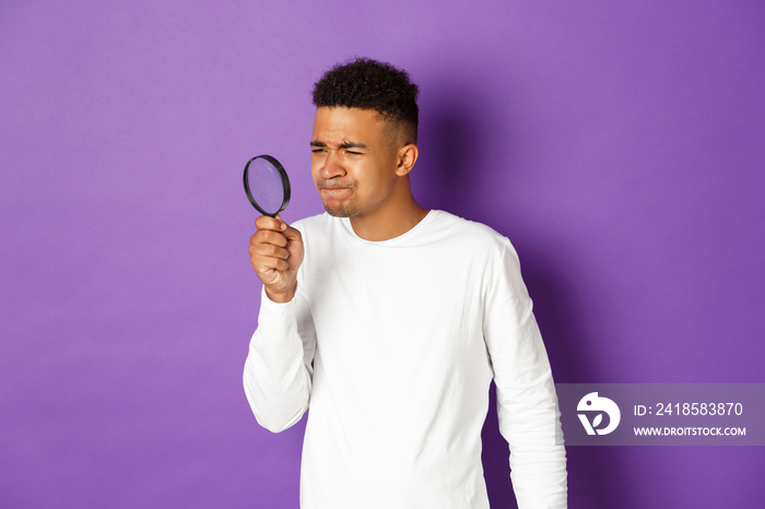 Image of young african-american male student looking for something with magnifying glass, squinting 