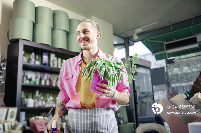 Positive delighted blonde man holding violet flower pot