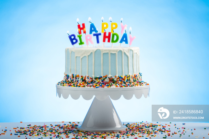 Blue Birthday Cake with Sprinkles on a White Cake Plate and Blue Background with Happy Birthday cand