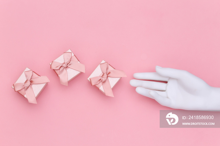 White mannequin hand and gift boxes on pink background. Top view